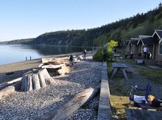 people are standing on the beach by some trees and houses with picnic tables in front of them