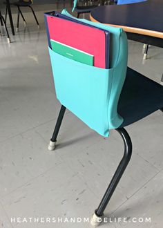 a school desk with a blue chair and pink folders in the pocket on it