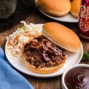 two pulled pork sandwiches on buns with coleslaw and ketchup next to them