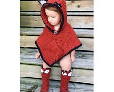 a small child wearing a red and black crochet hooded ponchy with fox ears