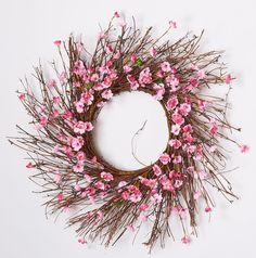 a wreath made out of branches with pink flowers on the top and bottom, sitting on a white surface