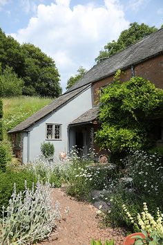 the house is surrounded by greenery and flowers in front of blue sky with white clouds