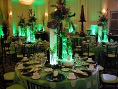 the tables are set up for an event with green lighting and tall centerpieces