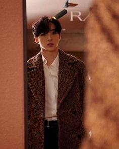 a man standing in front of a mirror wearing a coat and white button up shirt