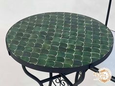 a table with green tiles on it and a round metal frame around the top, sitting on a white floor