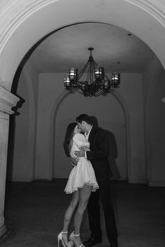 black and white photograph of a couple kissing in an archway with chandelier overhead