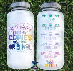 two water bottles sitting in the grass with words painted on them, one is white and the other is blue