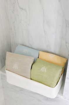 three folded towels sitting on top of a white shelf next to a marble tiled wall