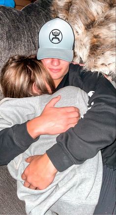 a man and woman cuddling on a couch with a dog wearing a hat over their heads