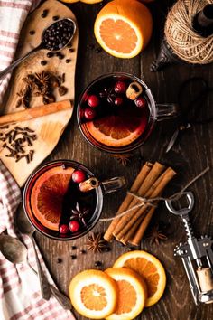 two glasses of mulled with orange slices and cinnamons on a wooden table surrounded by other ingredients