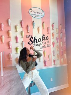 a woman sitting on a stool in front of a wall with pink and blue stripes