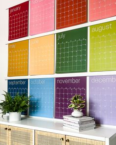 a colorful calendar is on the wall above a white table with books and a potted plant