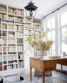 a vase with flowers on a table in front of a bookshelf