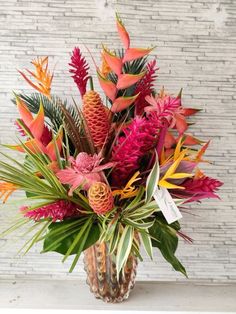 a vase filled with lots of colorful flowers on top of a white table next to a brick wall