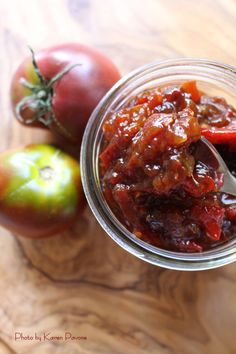 a jar filled with jam next to two tomatoes