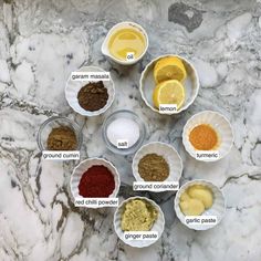 seven bowls with different ingredients in them on a marble counter top, labeled as glyphamin, turment, ground cumine, garlic paste, and lemon