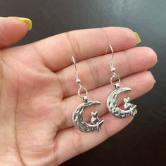 A pair of statement moon earrings has the power to elevate your everyday look. This unique cat and moon earring design looks gorgeous paired with any casual or dressy outfit.  ● 17.3mm 925 sterling silver fish hook  ● 20mm alloy moon charm  ● Made with hypoallergenic material * Please note for health and safety purposes and quality control these earrings are final sale Please DM me with any questions. ABOUT ABBYANDCO JEWELRY✨ 💖All abbyandco pieces are made with hypoallergenic gold plated and st Whimsical Silver Hypoallergenic Earrings, Whimsical Silver Metal Earrings, Whimsical Moon Charm Earrings Gift, Silver Cat Design Dangle Earrings, Cat And Moon, Moon Earring, Dressy Outfit, Celestial Earrings, Silver Fish