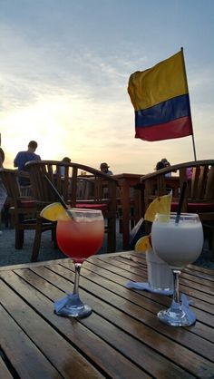 two drinks sitting on top of a wooden table next to each other with a flag in the background