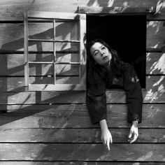 a black and white photo of a woman leaning against a wooden wall with her hand on the window sill