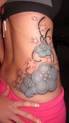 a woman's stomach with blue flowers on the side and an artistic tattoo design