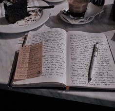 an open book with writing on it sitting next to a cup of coffee and cake