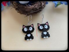 two black and white cat beaded earrings sitting on top of a table next to a bird nest