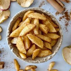 a bowl filled with sliced apples next to cinnamon sticks and an apple peel on the table