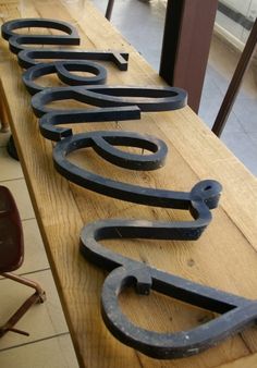 several metal letters are lined up on a wooden table with chairs in the back ground