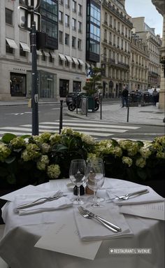 the table is set with silverware and wine glasses on it in front of an empty street