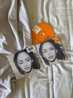 two cd's sitting on top of a bed next to each other with an orange disc in the background