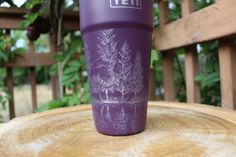 a purple yeti cup sitting on top of a wooden table next to a tree