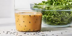 two glass bowls filled with salad dressing on top of a white table next to another bowl full of salad