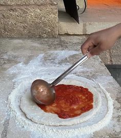 a person is using a ladle to make pizza dough on a plate with sauce