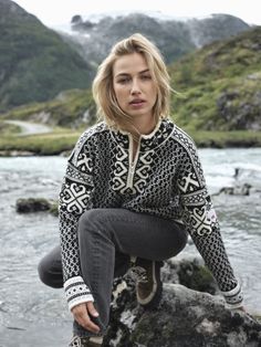 a woman sitting on top of a rock next to a river