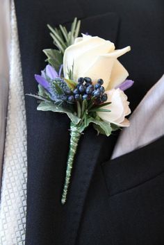 a boutonniere with white roses and blue berries is on the lapel of a man in a tuxedo