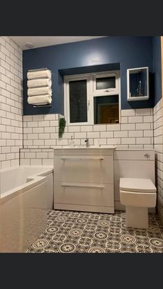 a white toilet sitting next to a bath tub in a bathroom under a window on top of a tiled floor