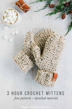 three crochet mittens on top of a white table with cinnamons and marshmallows