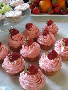 several cupcakes with pink frosting and strawberries on the top are arranged in rows