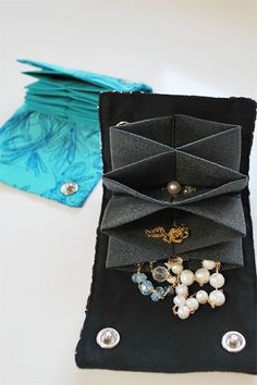 an open black case with pearls and brooches on it next to a folded blue napkin