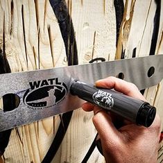 a person holding a knife in front of a wooden wall with the words wattl on it