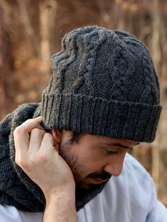 a man in a hat and scarf is holding his hand to his ear while looking down