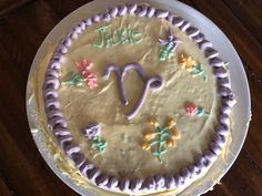 a cake decorated with icing and flowers on a white plate sitting on a wooden table