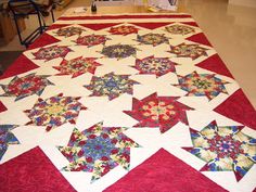 a quilted table topper on a red and white table cloth with flowers in the center