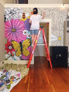 a person on a ladder painting a flowered wall with flowers and butterflies in the background