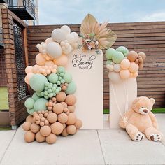 a teddy bear sitting in front of a sign with balloons attached to it's sides