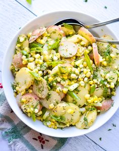 a white bowl filled with potatoes, corn and seasoning on top of a table