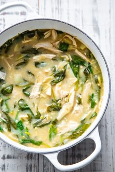 a pot filled with chicken and spinach soup on top of a white wooden table