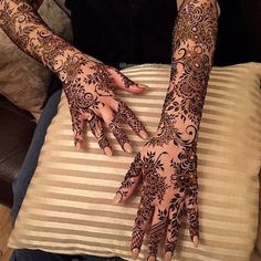 two hands with henna tattoos on them sitting next to a brown pillow and pillows