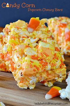 a pile of candy cornflakes on top of a wooden cutting board next to carrots