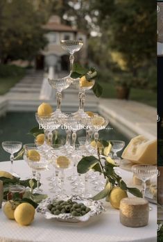 a table topped with lots of wine glasses and lemons next to a fountain filled with water